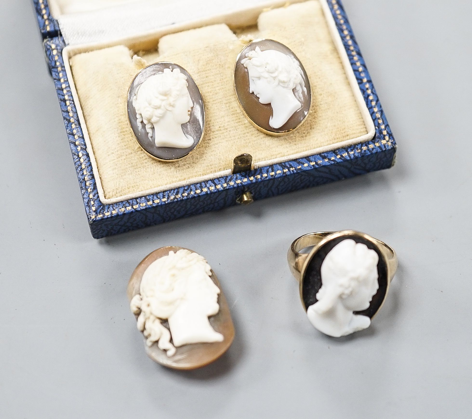 A yellow metal and hardstone set cameo ring, size J (a.f.), gross 6.9 grams, a pair of similar cameo shell ear clips and one other cameo shell mount.